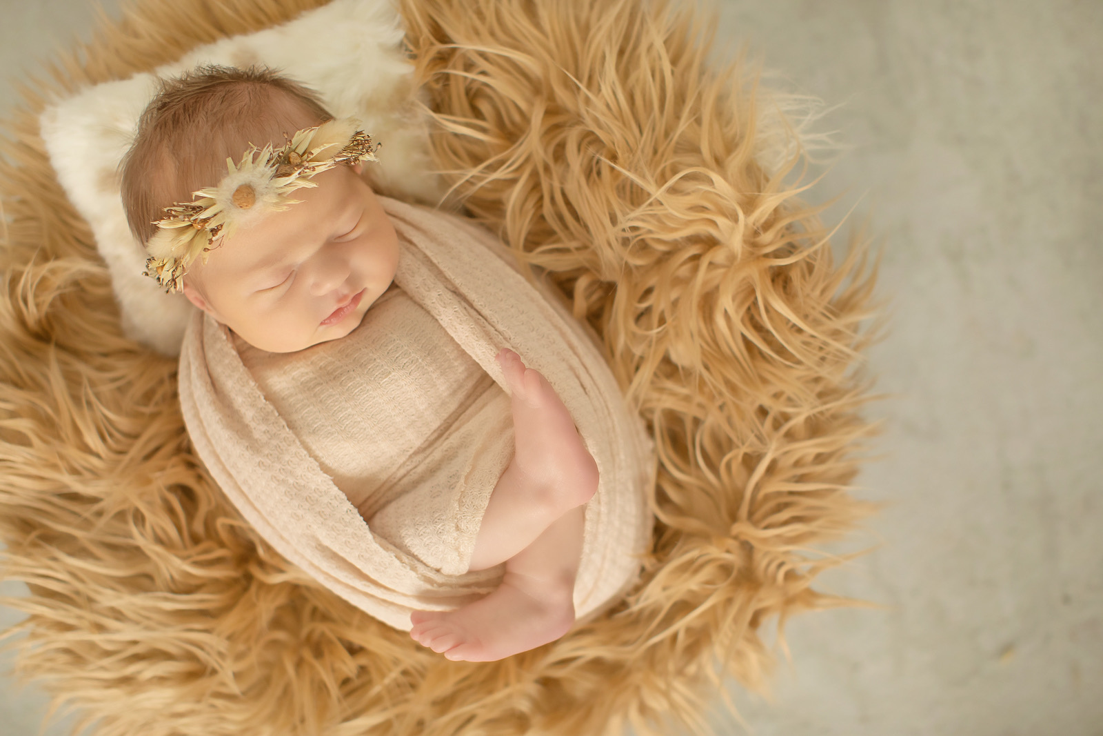 Newborn with dried-flower crown on tan fur