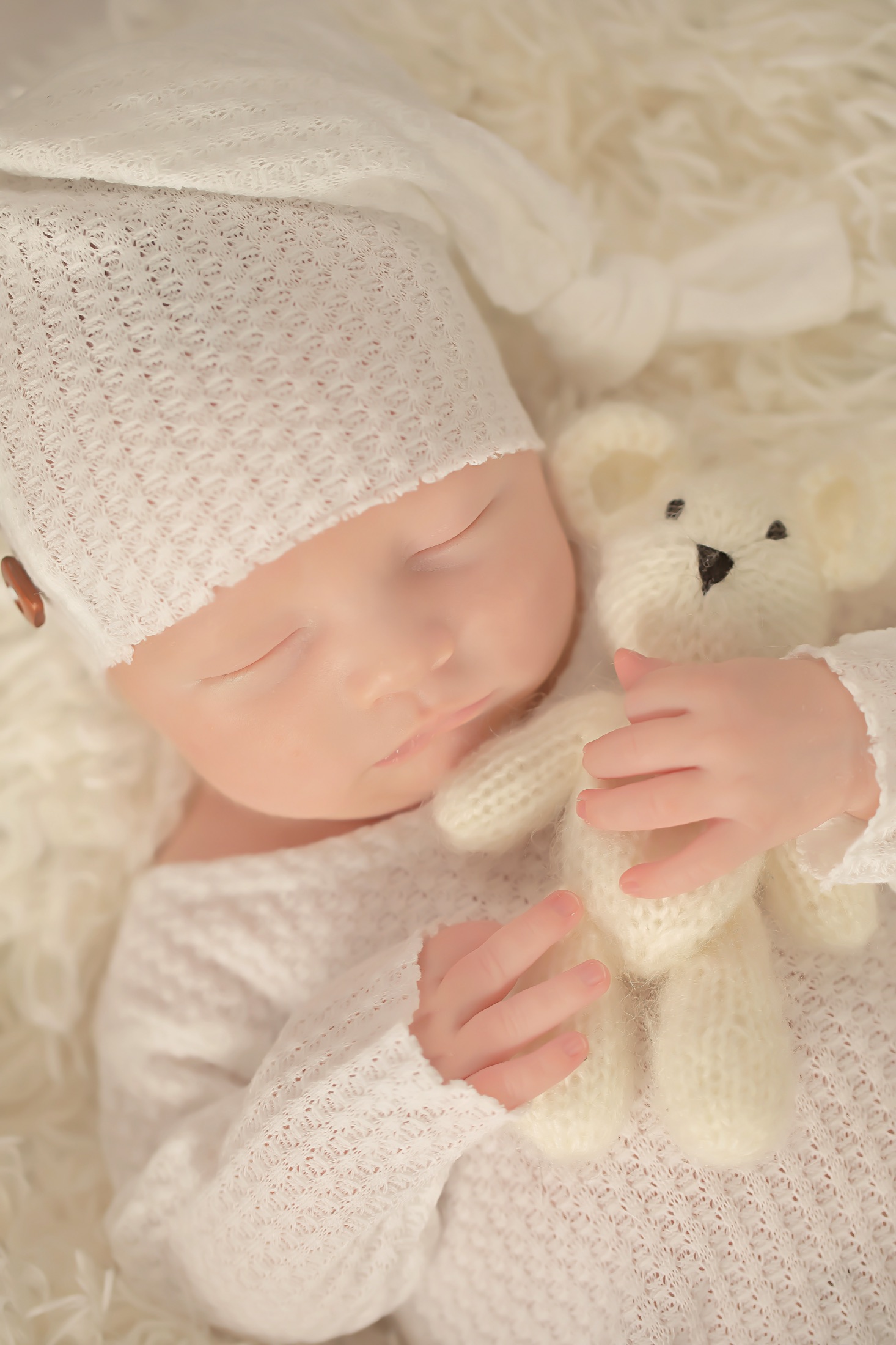 Newborn in white knit holding a teddy bear